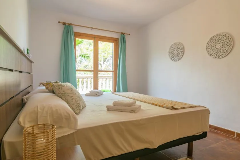 A bedroom with a bed facing a glass door framed by teal curtains.