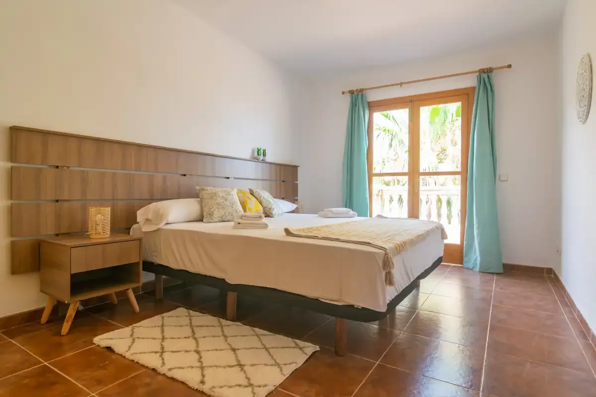 A bedroom with a bed beside a bright window and teal curtains.