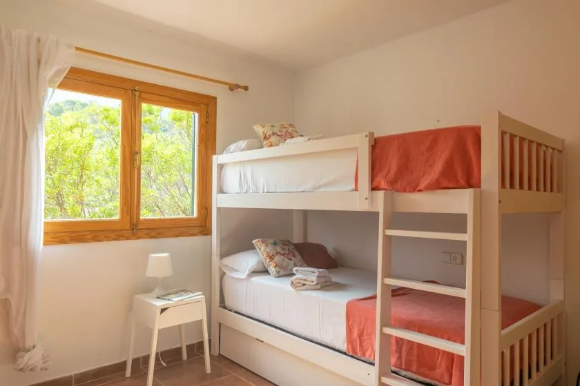 A bright bedroom with a wooden bunk bed and a window overlooking greenery.
