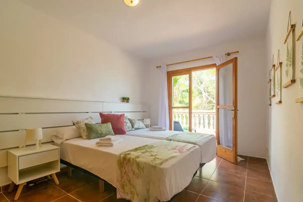 A bright bedroom with a bed beside an open balcony door.