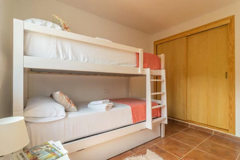 A bunk bed with white bedding and coral accents stands beside wooden closet doors.