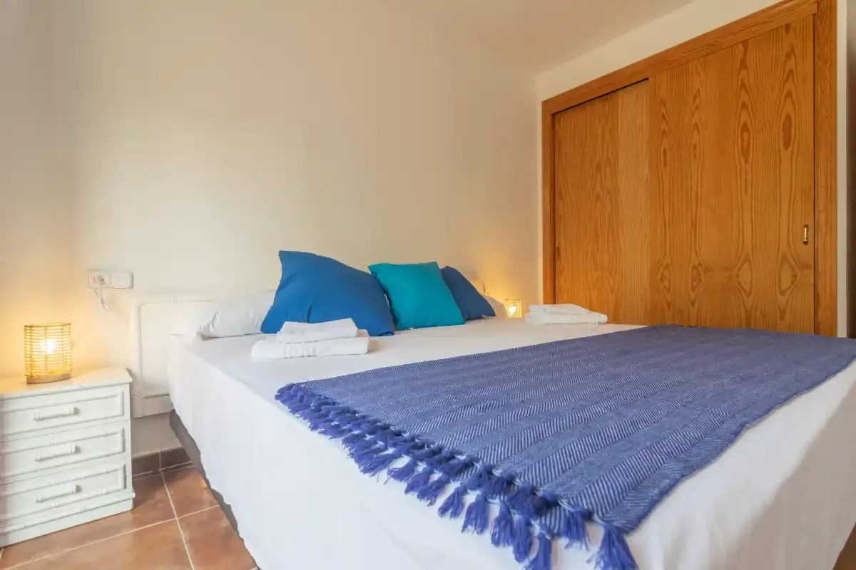 A bedroom with white bedding, colorful pillows, and a blue throw.