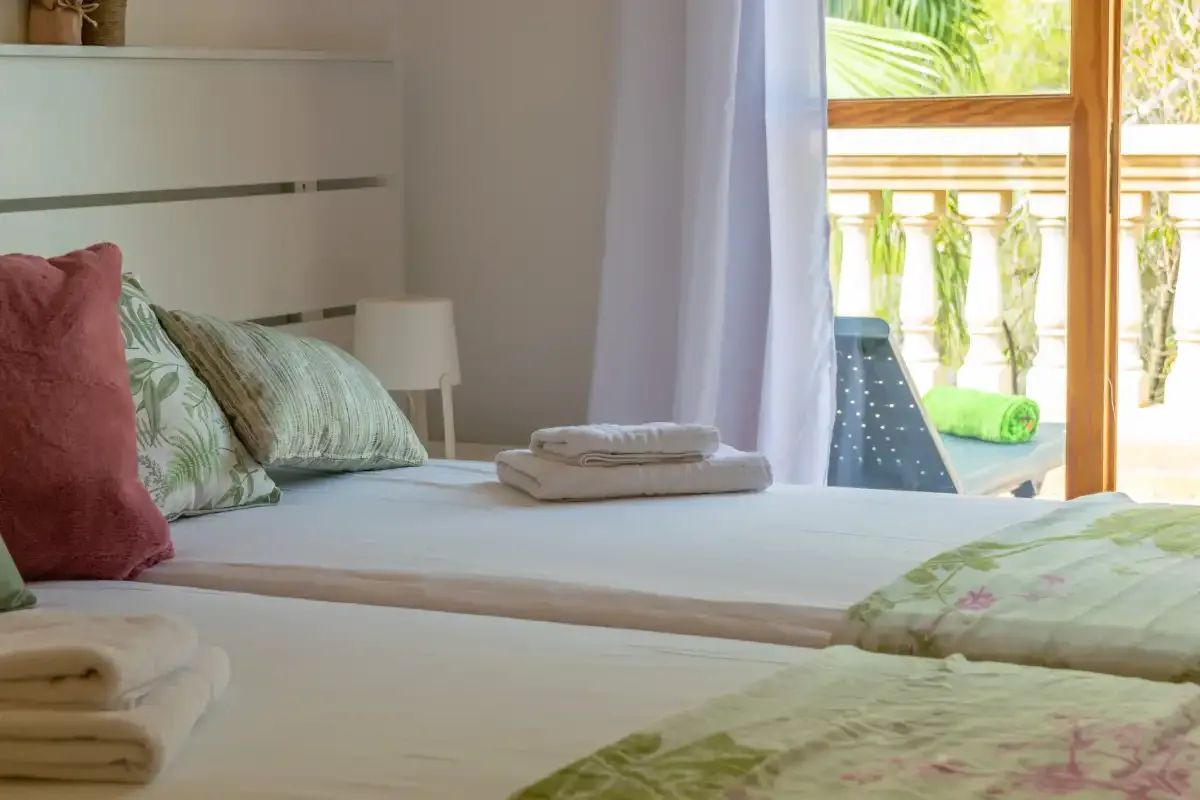 A bedroom with neatly made beds and a bright window overlooking greenery.