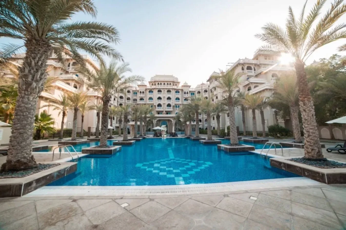 A large outdoor pool sits among palm trees in front of a resort building.