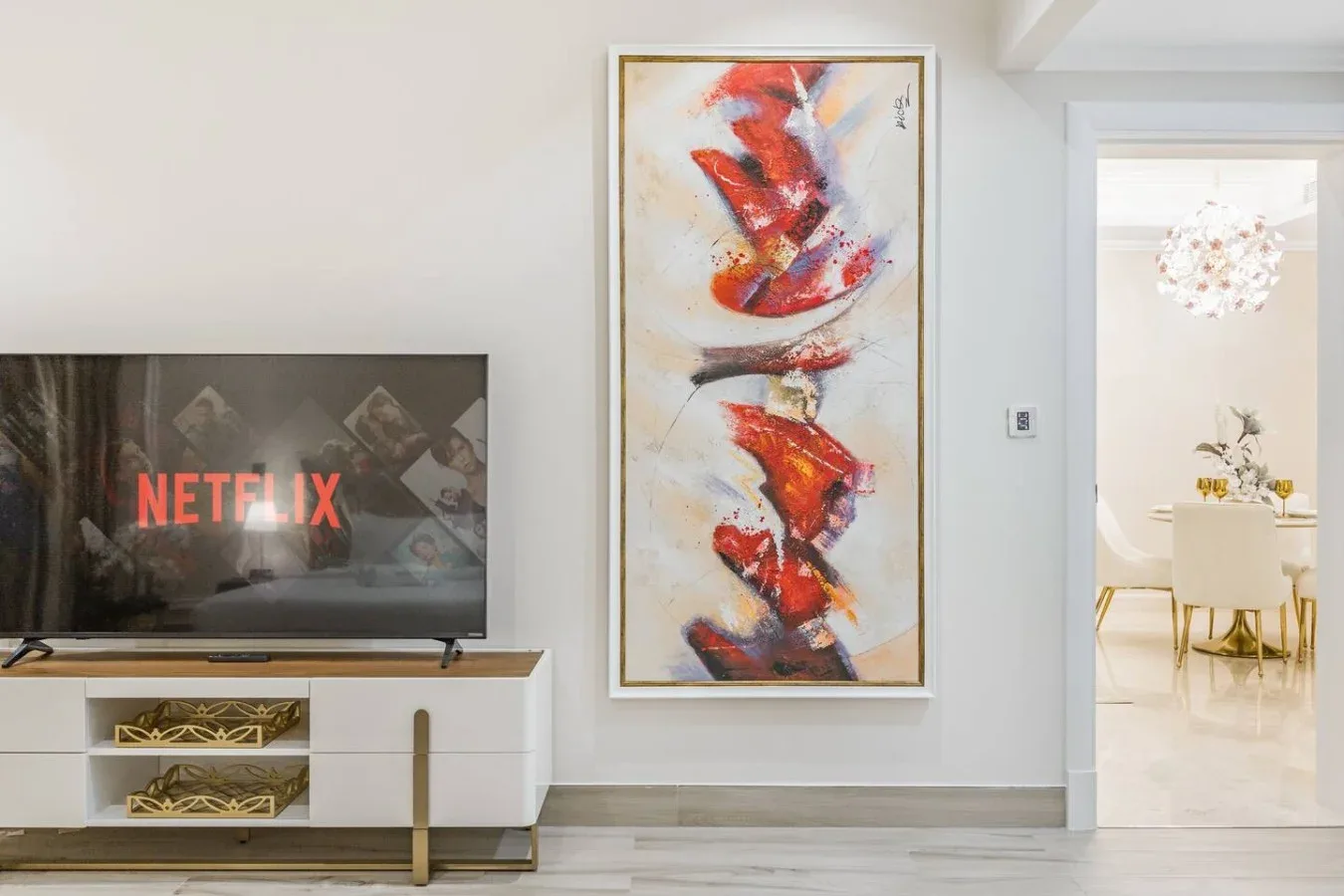 A bright living area with a television, abstract artwork, and an adjacent dining space.