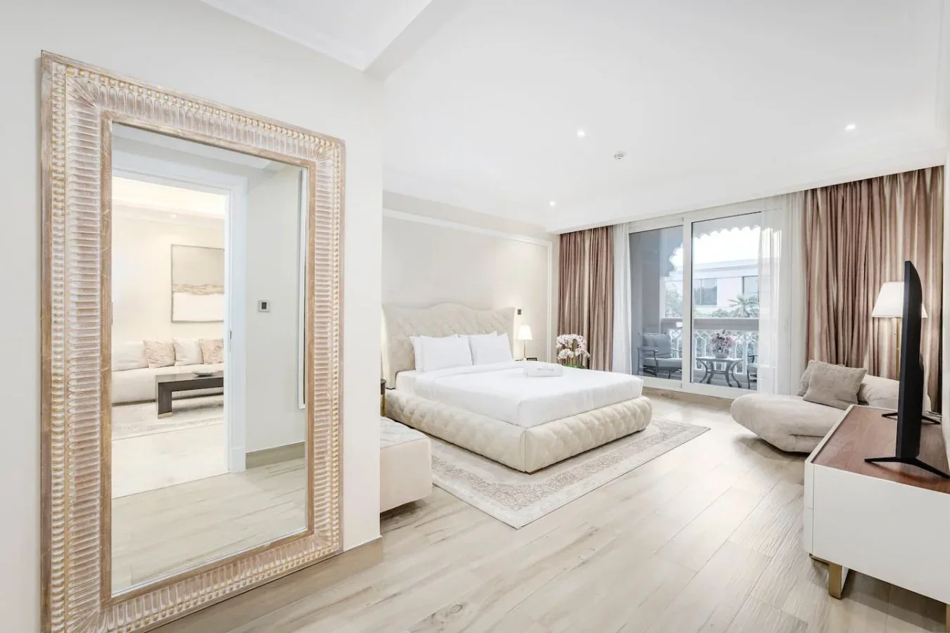 A bright bedroom with a large bed, neutral furnishings, and sliding glass doors.