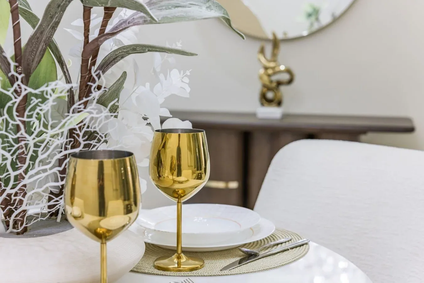A dining table is set with plates, cutlery, and gold-colored goblets.