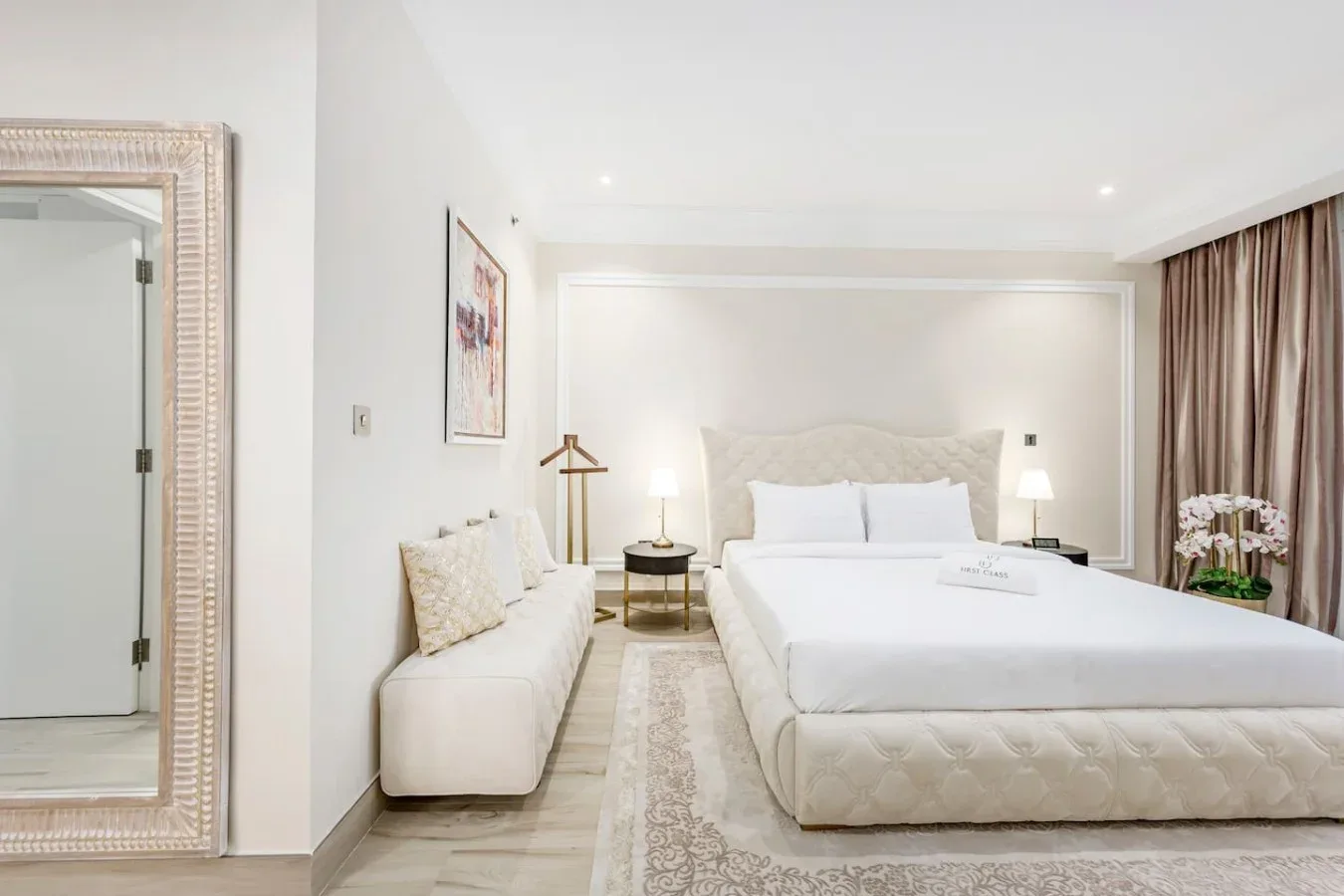 A bright bedroom features a large bed, a small seating area, and curtains.