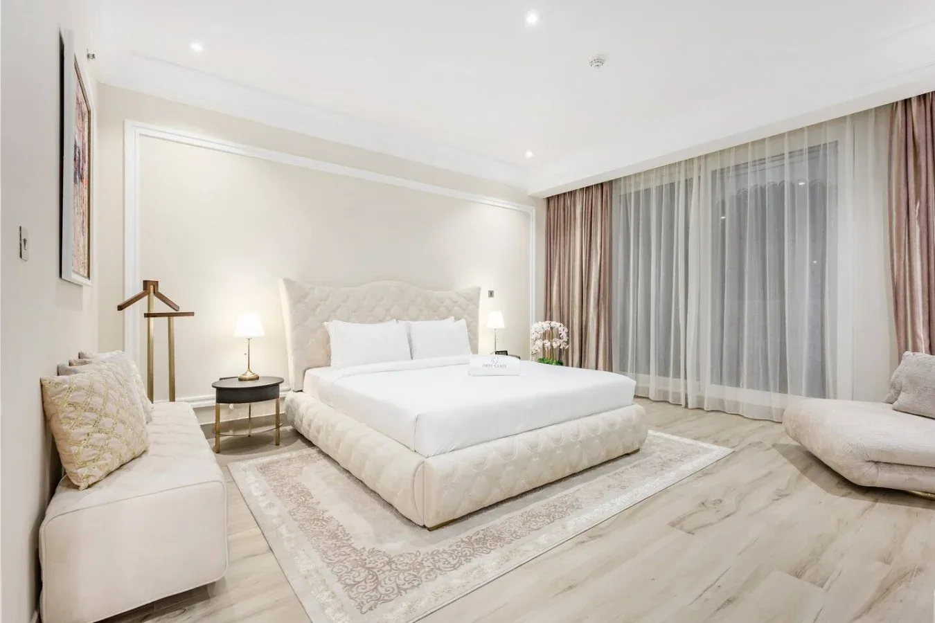 A bright bedroom with a large bed beside floor-to-ceiling curtains.