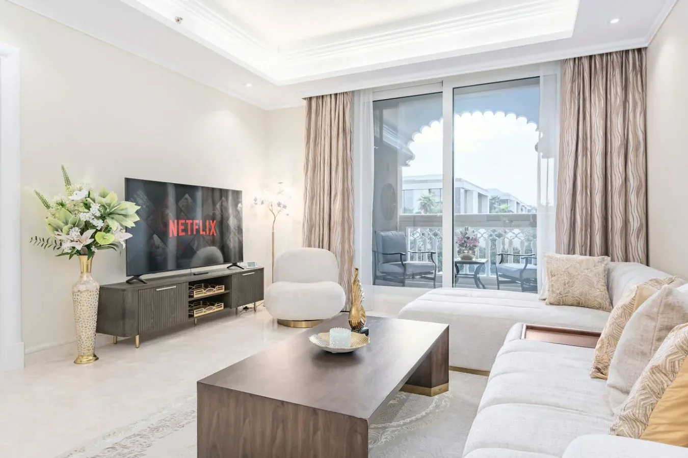 A bright living room with seating, a coffee table, and glass doors opening onto a balcony.