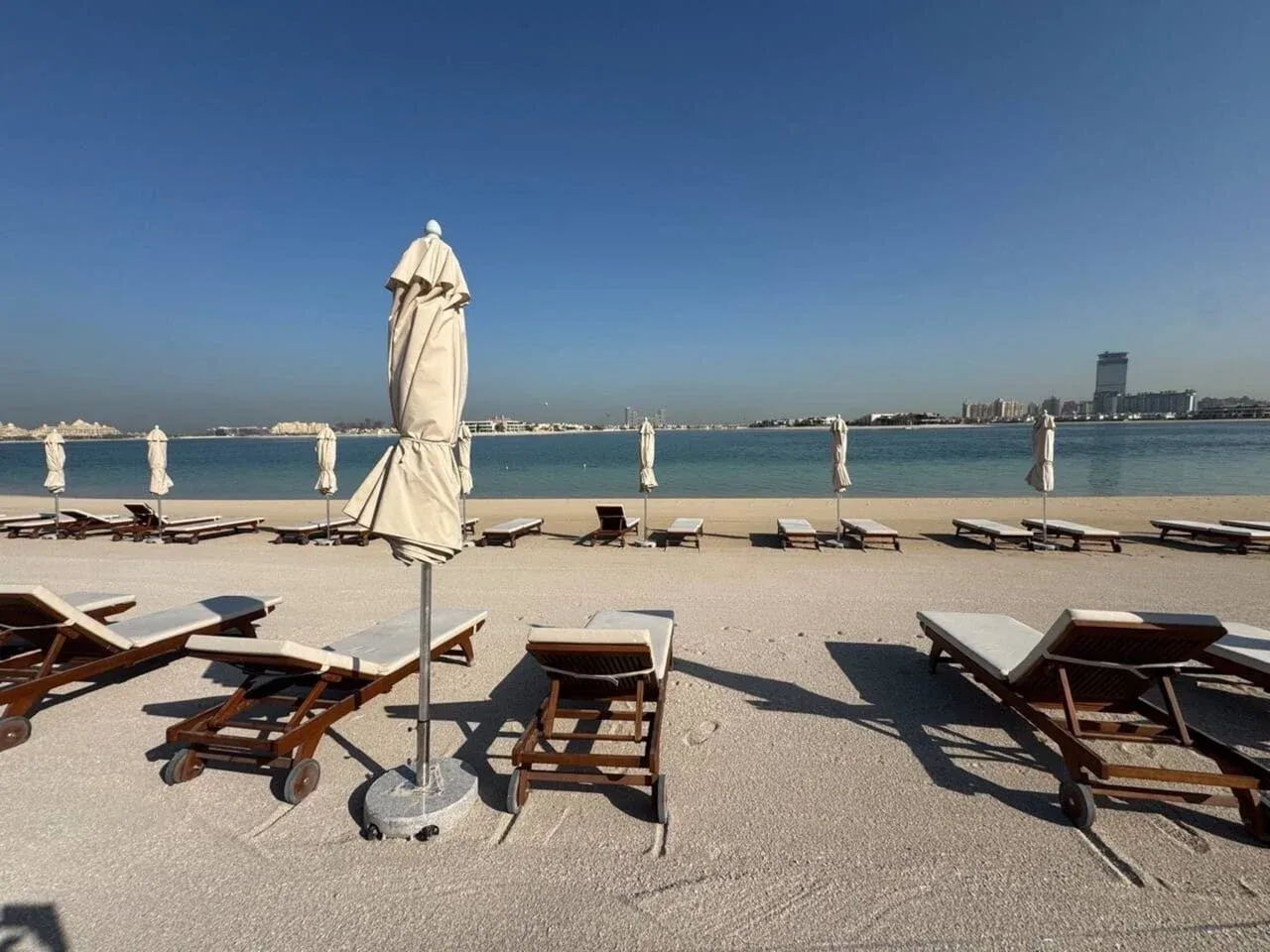 A beachside seating area with lounge chairs and closed umbrellas overlooks calm water.