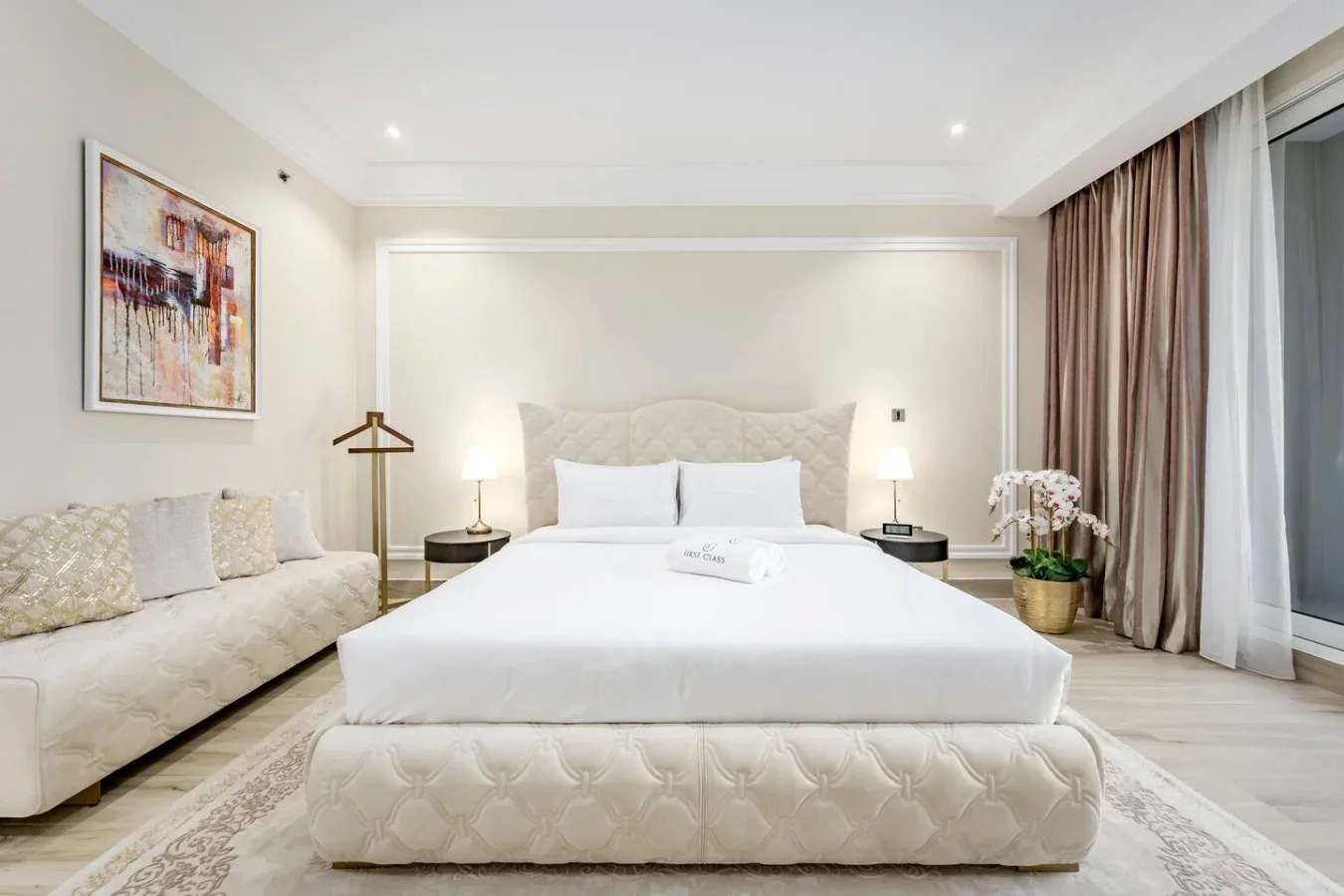 A bright bedroom with a large bed, bedside lamps, and a seating area.
