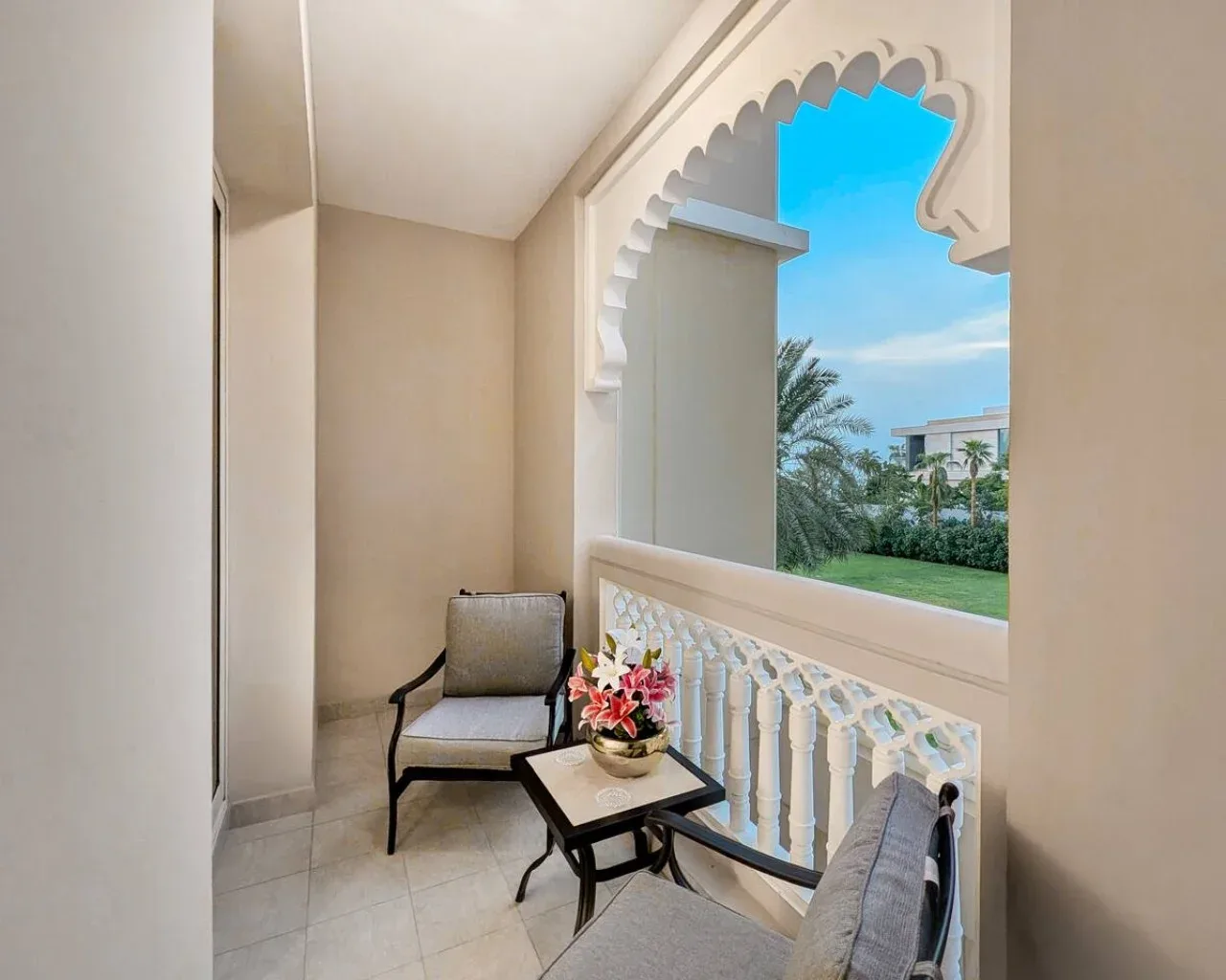 A covered balcony with seating and an ornate arched opening overlooking greenery.