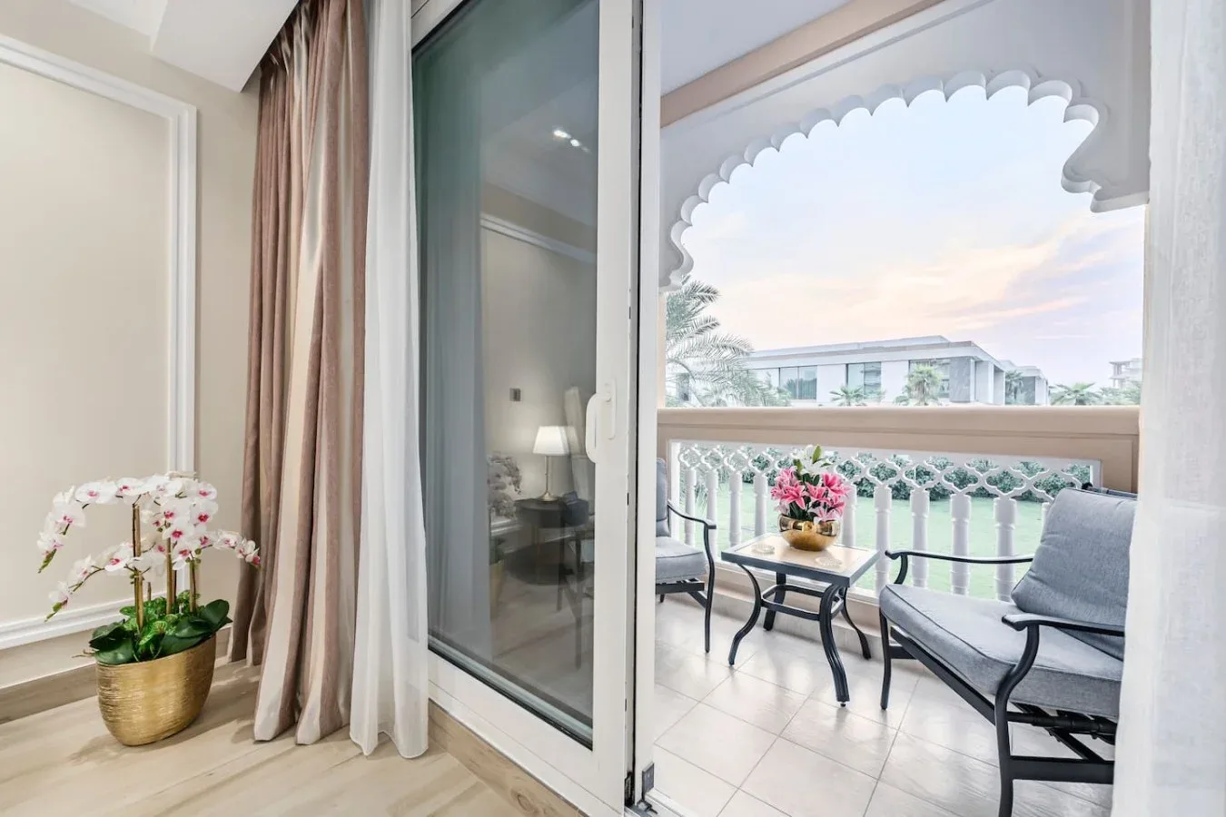 A sliding glass door opens onto a balcony with seating and potted flowers.
