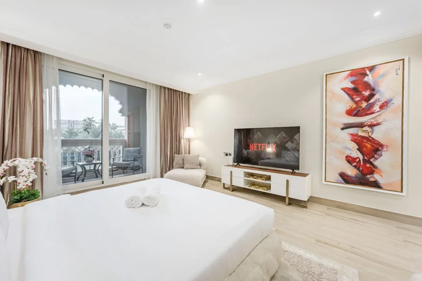 A bright bedroom with a large bed, a television, and sliding glass doors.