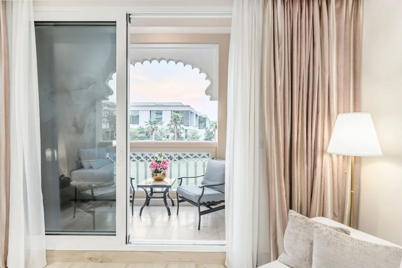 A bright bedroom opens onto a balcony with seating and a small table.