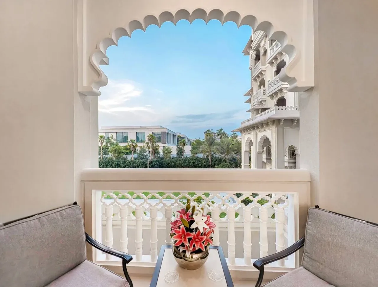 Una zona de estar en el balcón enmarca un arco ornamentado y edificios y palmeras cercanos.