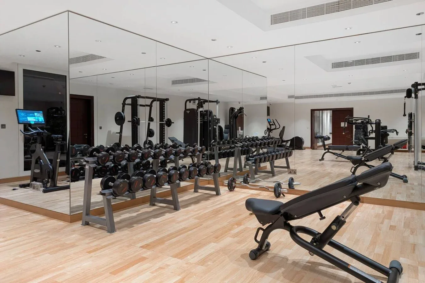 A mirrored gym with rows of weights and an adjustable exercise bench.