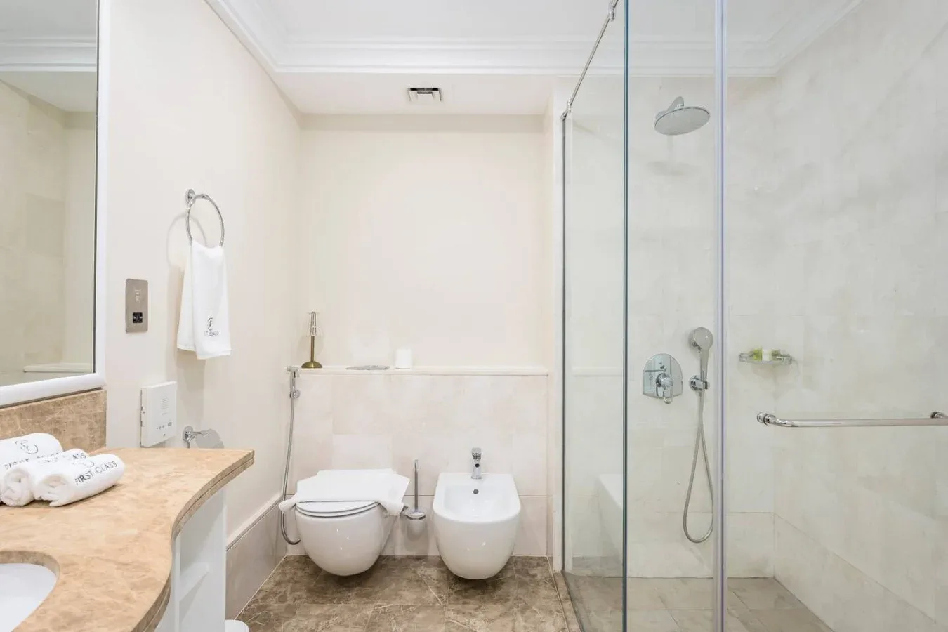 A bright bathroom with a stone counter, toilet, bidet, and glass shower.