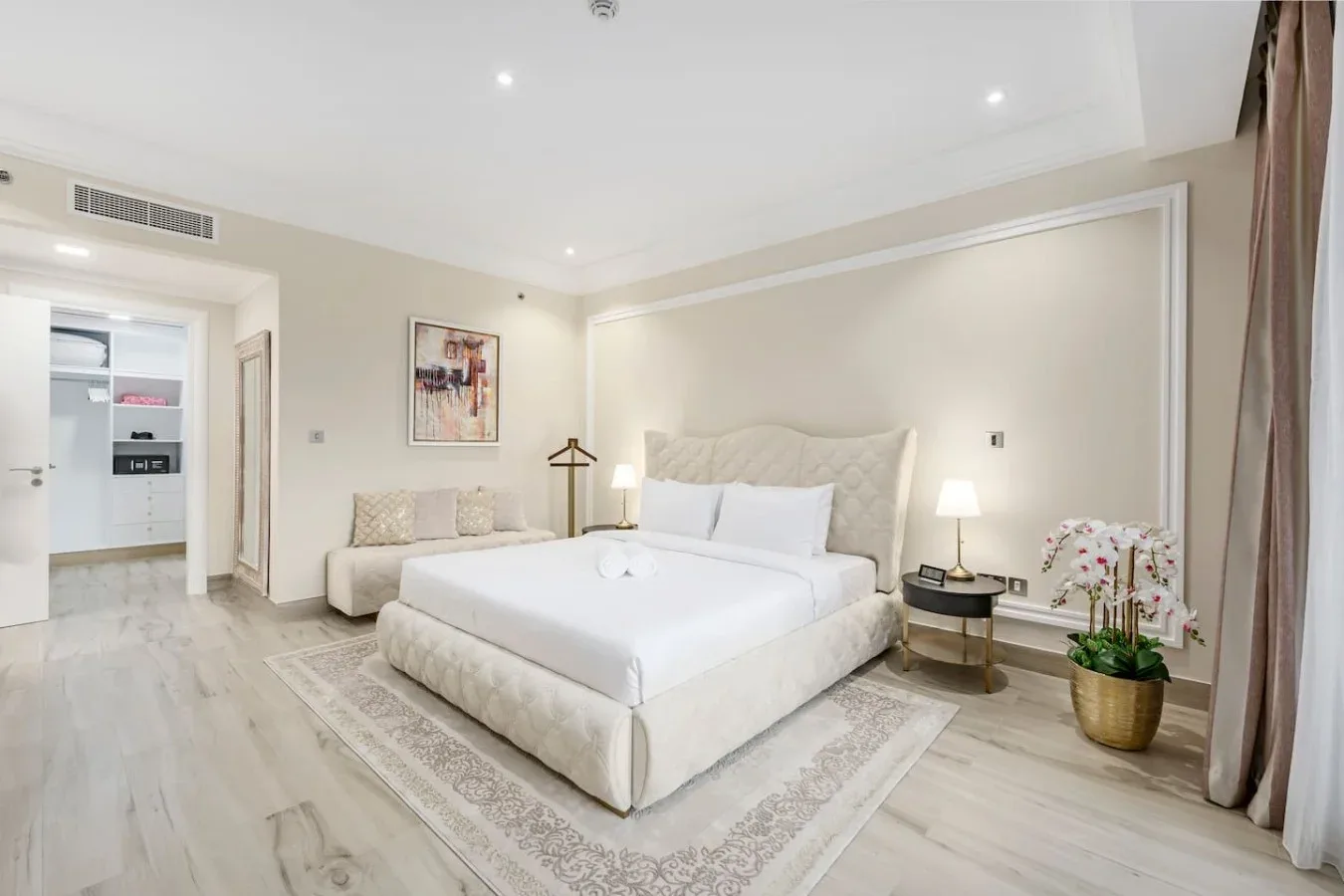 A bright bedroom with a large bed, bedside tables, and a small seating area.