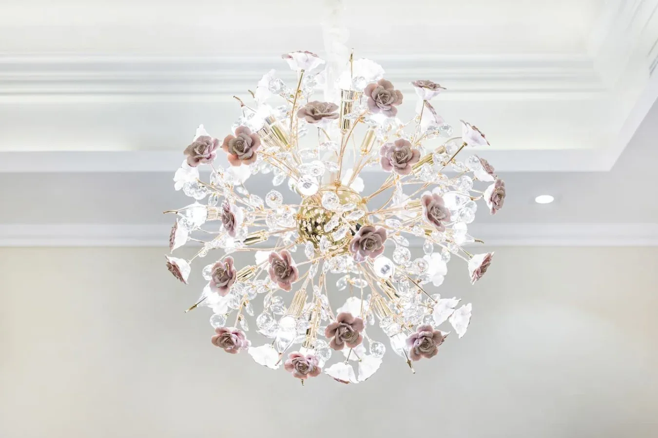 A decorative chandelier with floral details hangs from a white ceiling.
