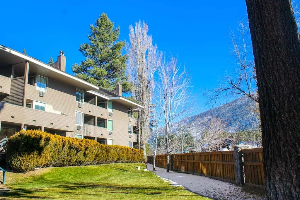 Un edificio residencial de varias viviendas está junto a un patio cercado y una montaña.