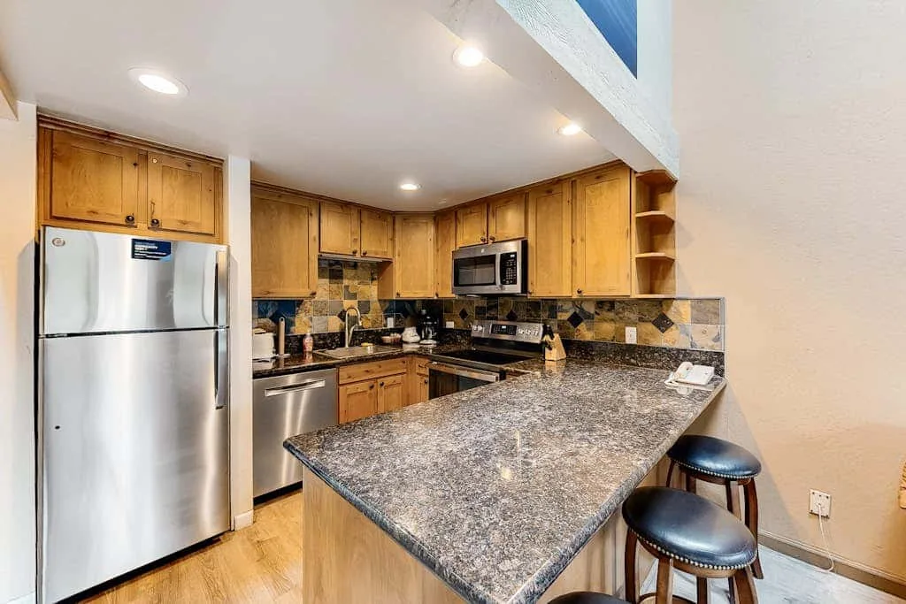 A kitchen with wooden cabinets, stainless steel appliances, and a large granite countertop.