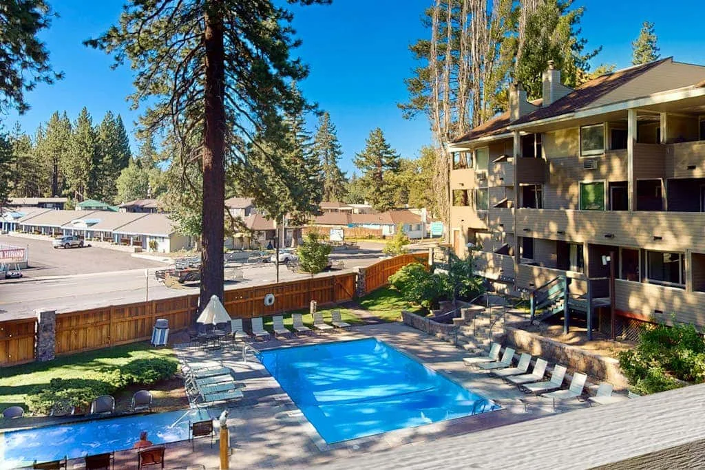 Una piscina al aire libre está junto a un edificio de varios pisos y árboles.