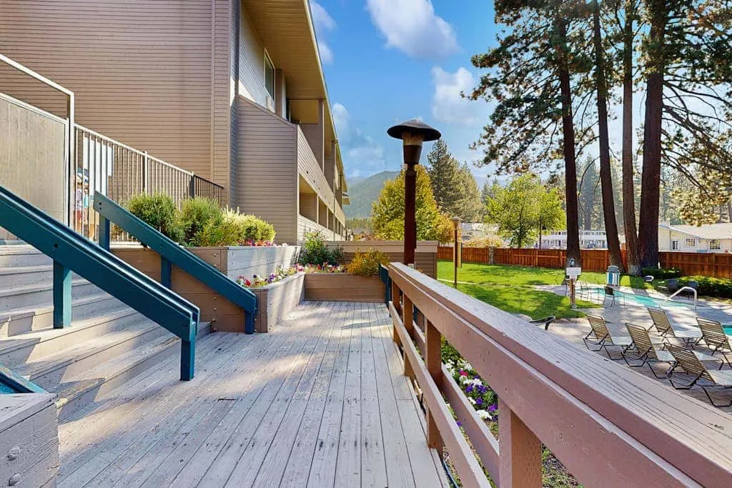 Una terraza de madera junto a un edificio da a una zona exterior ajardinada con asientos.