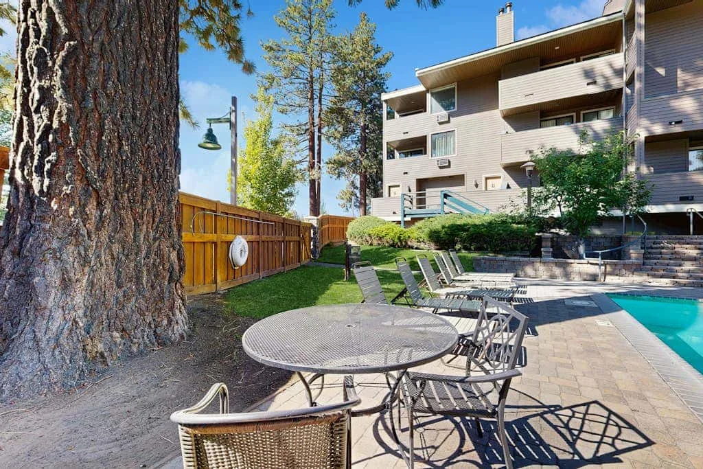 Un patio junto a una piscina al aire libre, con mesas y sillas metálicas junto a un edificio.