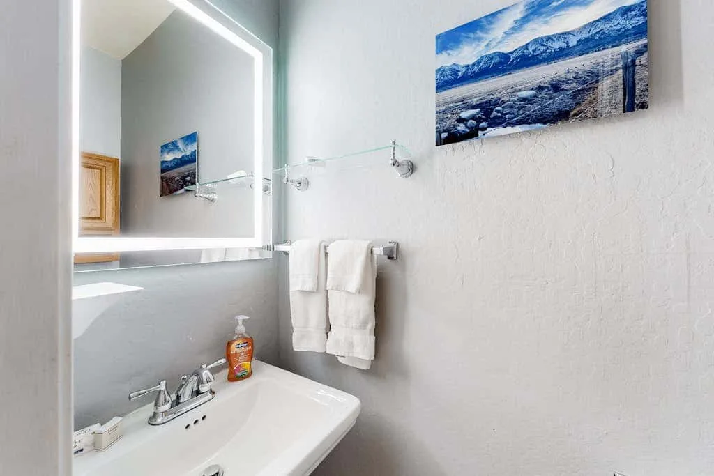 Un tocador de baño con espejo, toallas y un paisaje en la pared.
