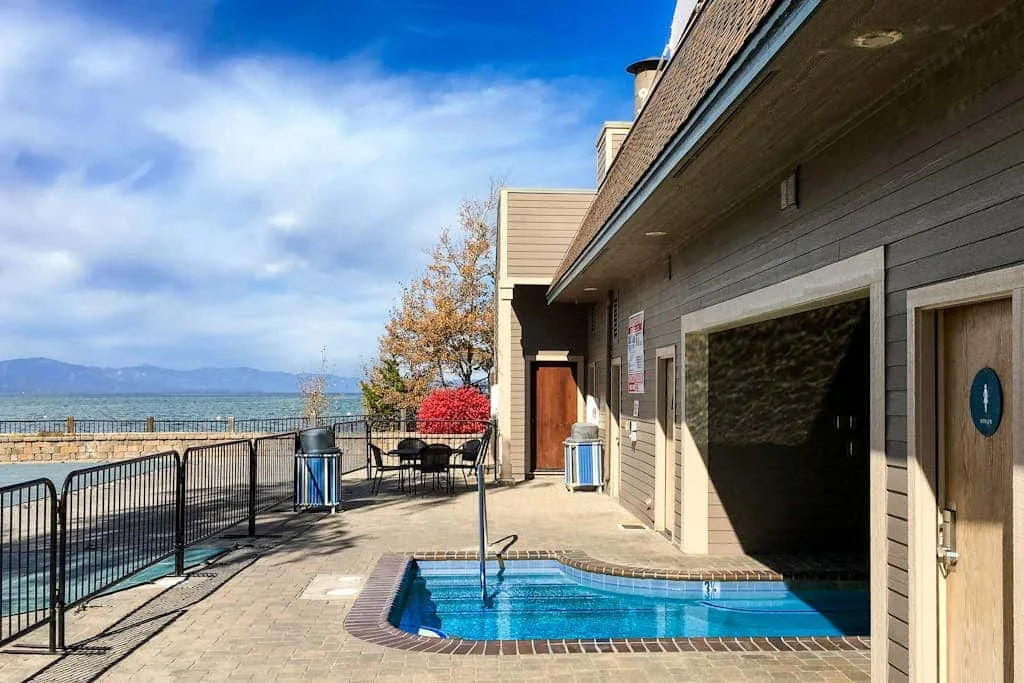 Una piscina al aire libre está junto a un patio frente al agua, con barandilla y vistas a las montañas.
