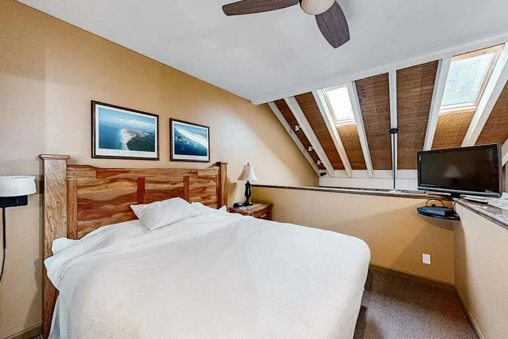 Un dormitorio con una cama bajo tragaluces inclinados y un televisor.