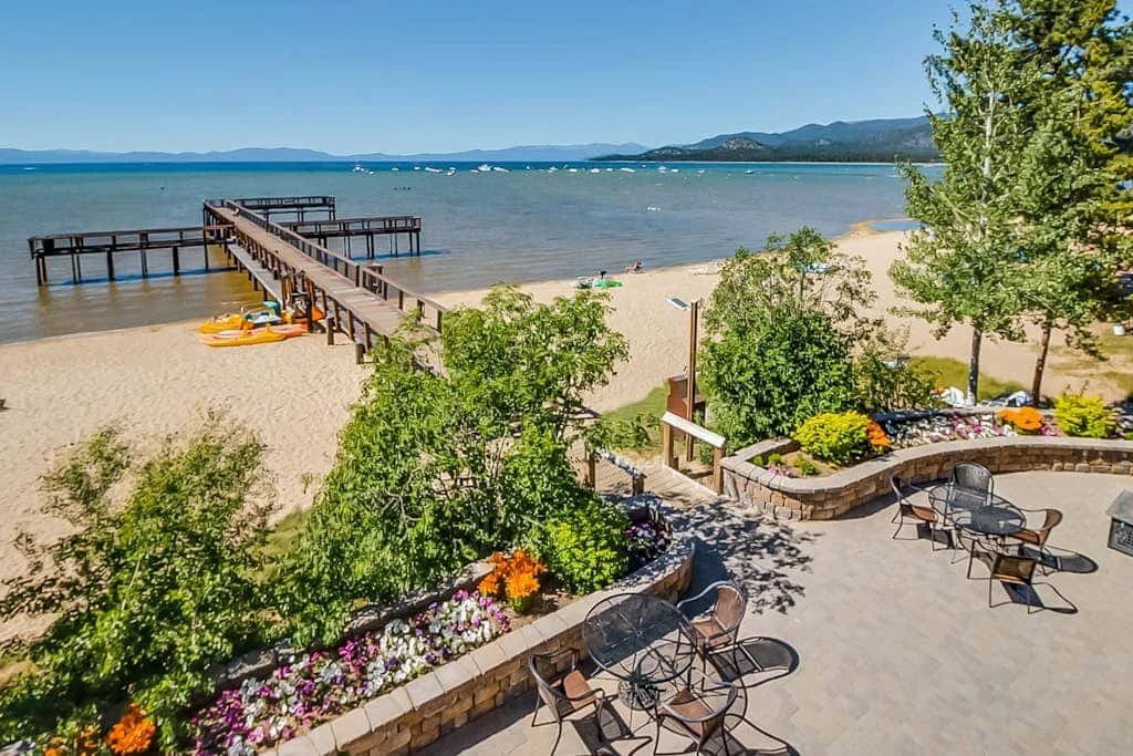 Un patio junto al lago da a una playa de arena y un muelle de madera.