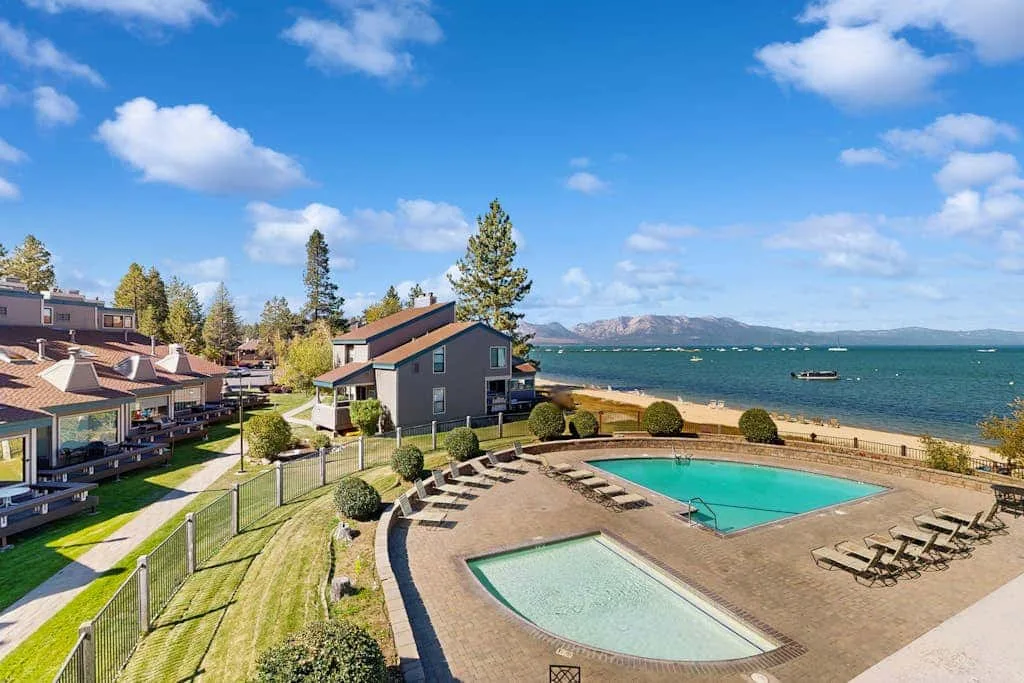 Zona de piscina al aire libre junto a varios edificios, con el lago al fondo.