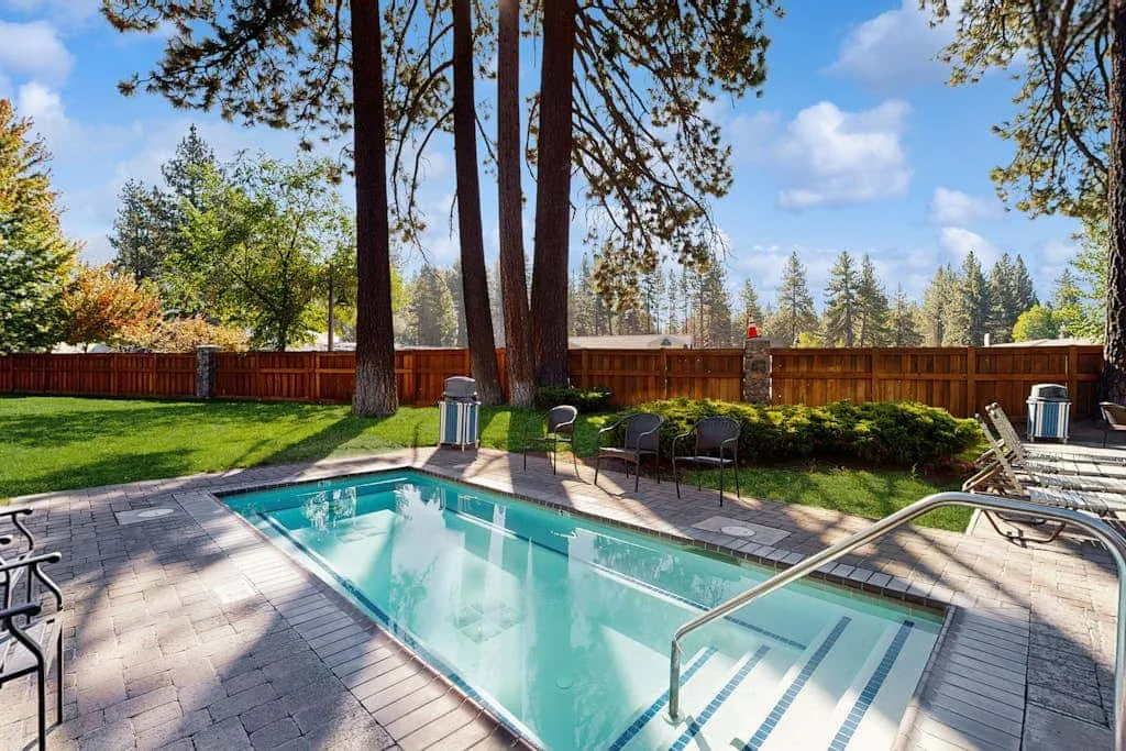 Una piscina al aire libre está junto a un patio pavimentado y un jardín.