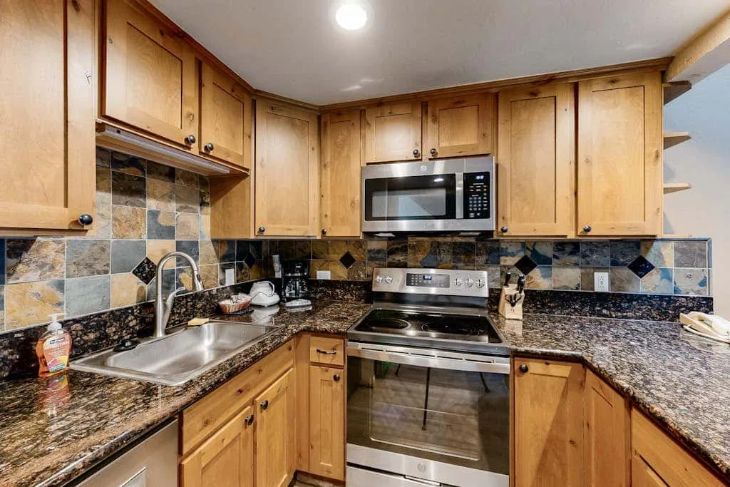 A kitchen with wooden cabinets, dark countertops, and stainless steel appliances.