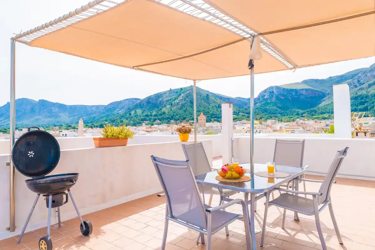 Una terraza en la azotea tiene asientos y una mesa bajo un toldo, con montañas a lo lejos.