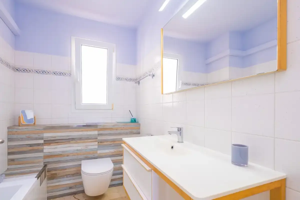 Un baño alicatado con bañera, inodoro y lavabo bajo un espejo.