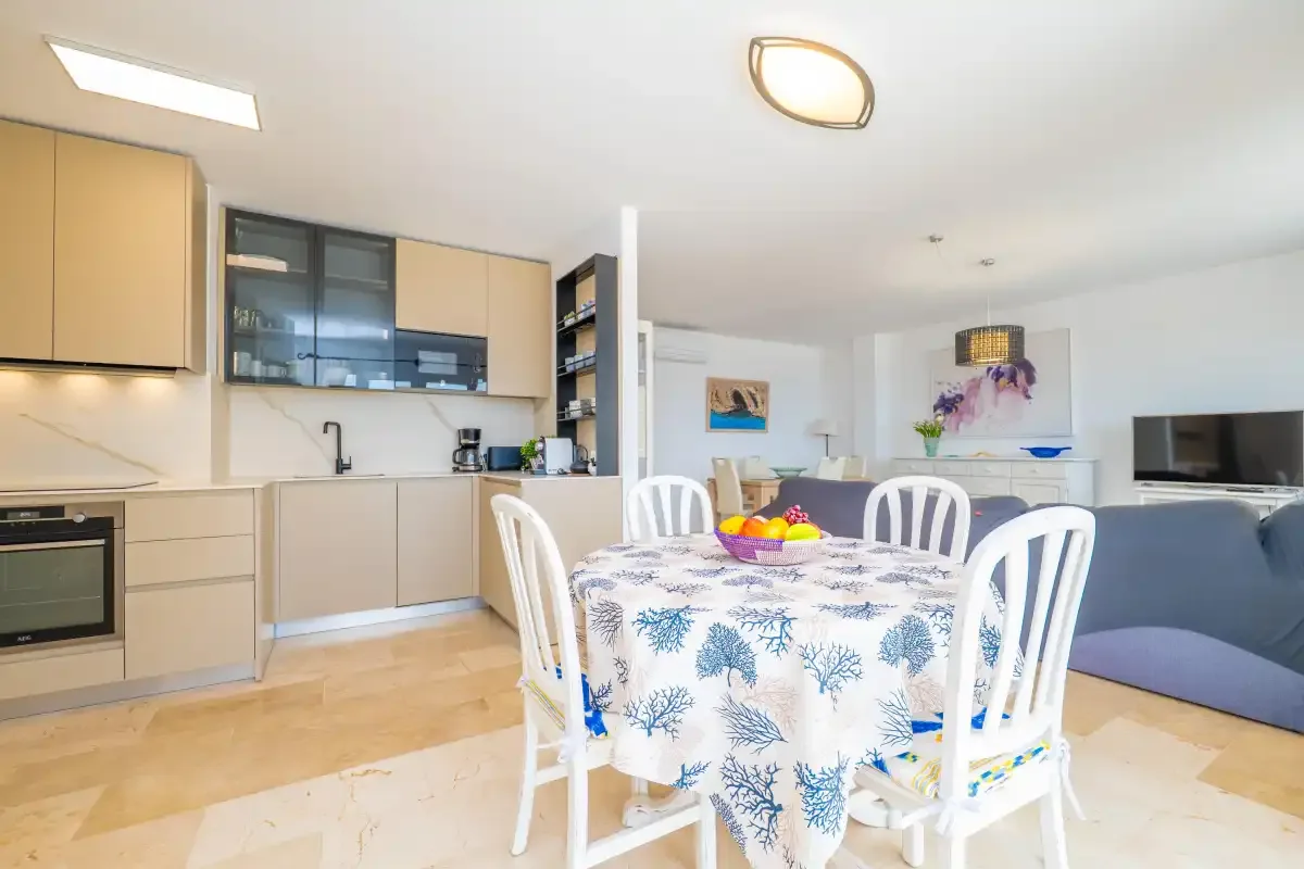 Una luminosa cocina y zona de comedor con un mantel estampado y asientos blancos.