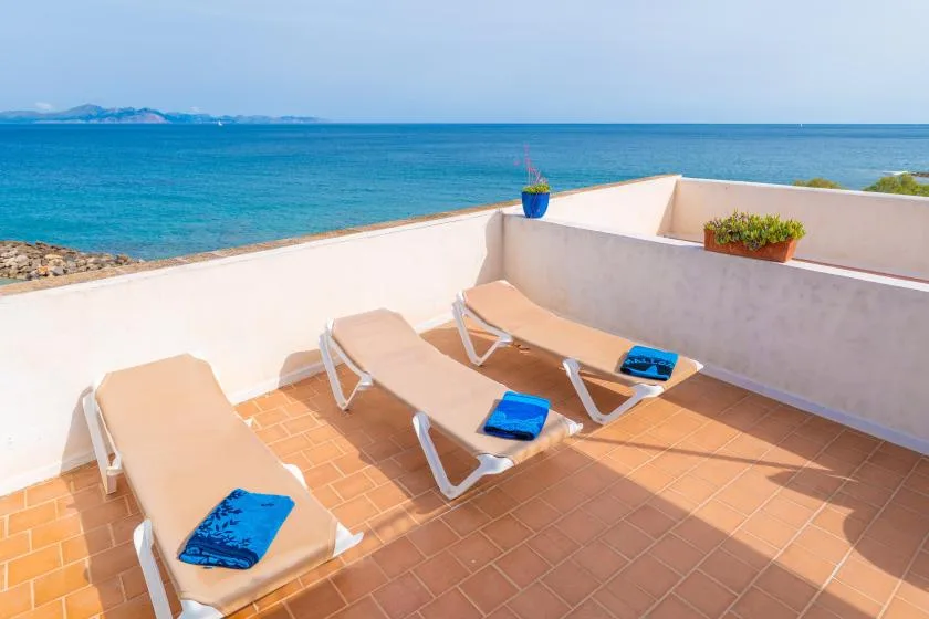Una terraza soleada con tumbonas y suelo de baldosas mira al mar.