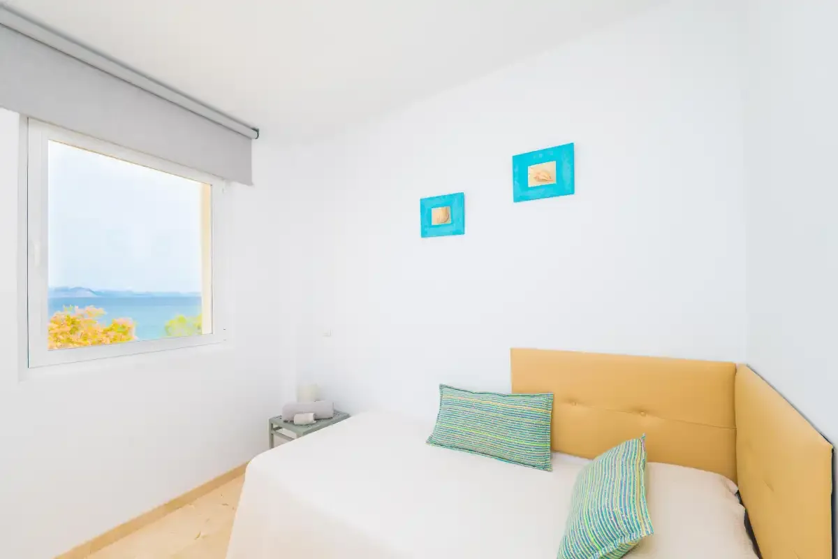 Un dormitorio con una cama, cojines de colores y una ventana con vistas al mar.