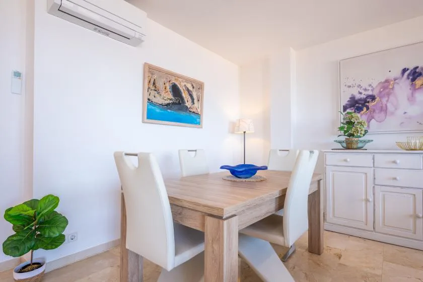 Un comedor con una mesa de madera, asientos blancos y arte colorido en la pared.