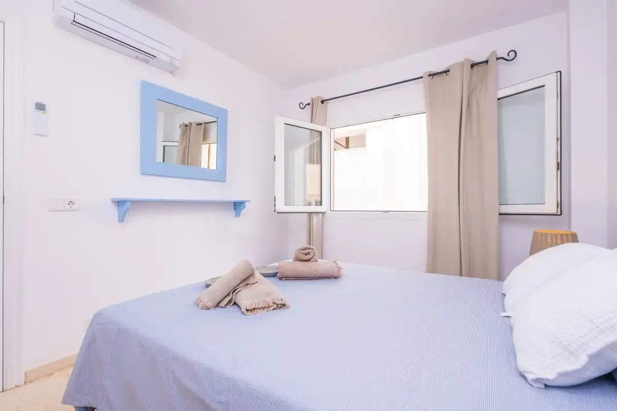 Un dormitorio luminoso con una cama, una ventana y aire acondicionado.