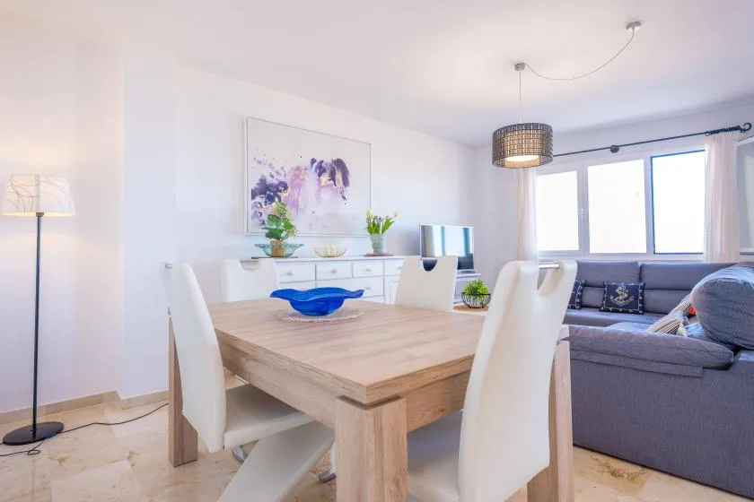 Un comedor y sala de estar luminosos con una mesa de madera y asientos grises.