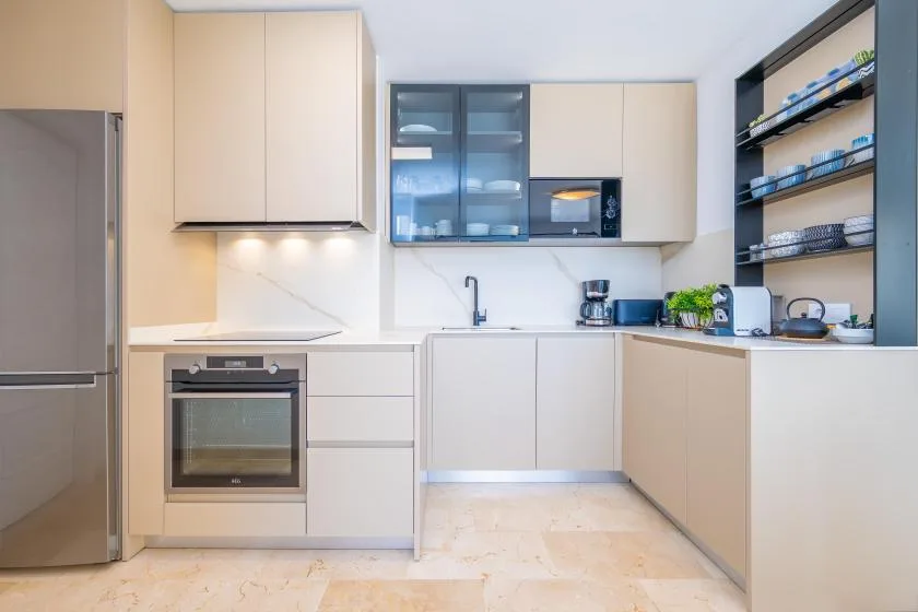 Una cocina moderna con gabinetes claros, horno integrado y estantes abiertos.