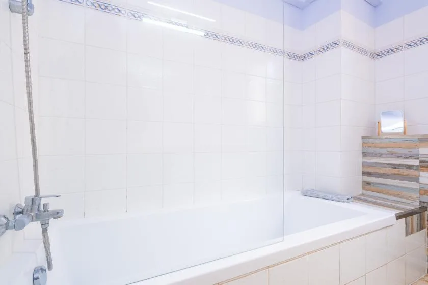 Un baño alicatado con bañera y grifería de ducha en la pared.
