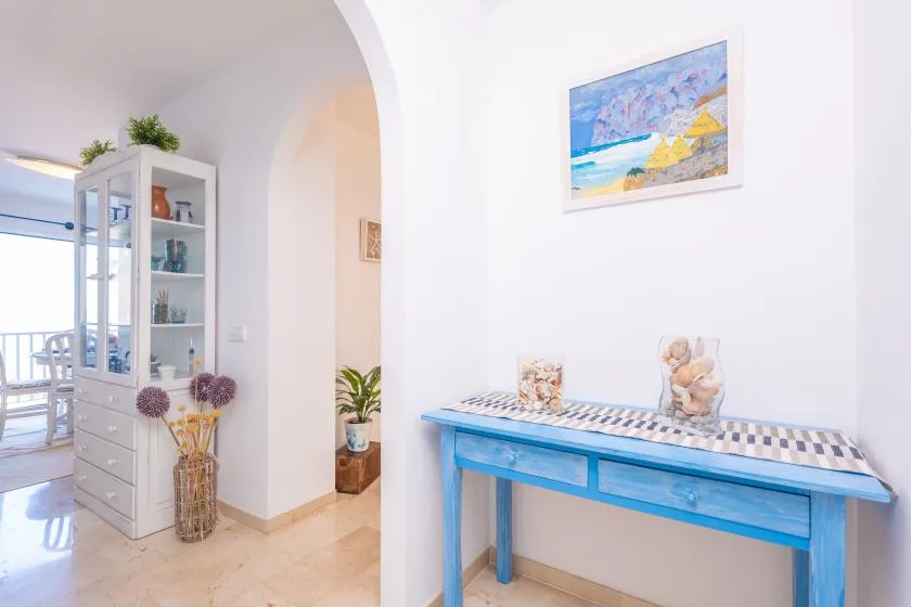 Un pasillo interior luminoso con una consola azul y arte enmarcado.