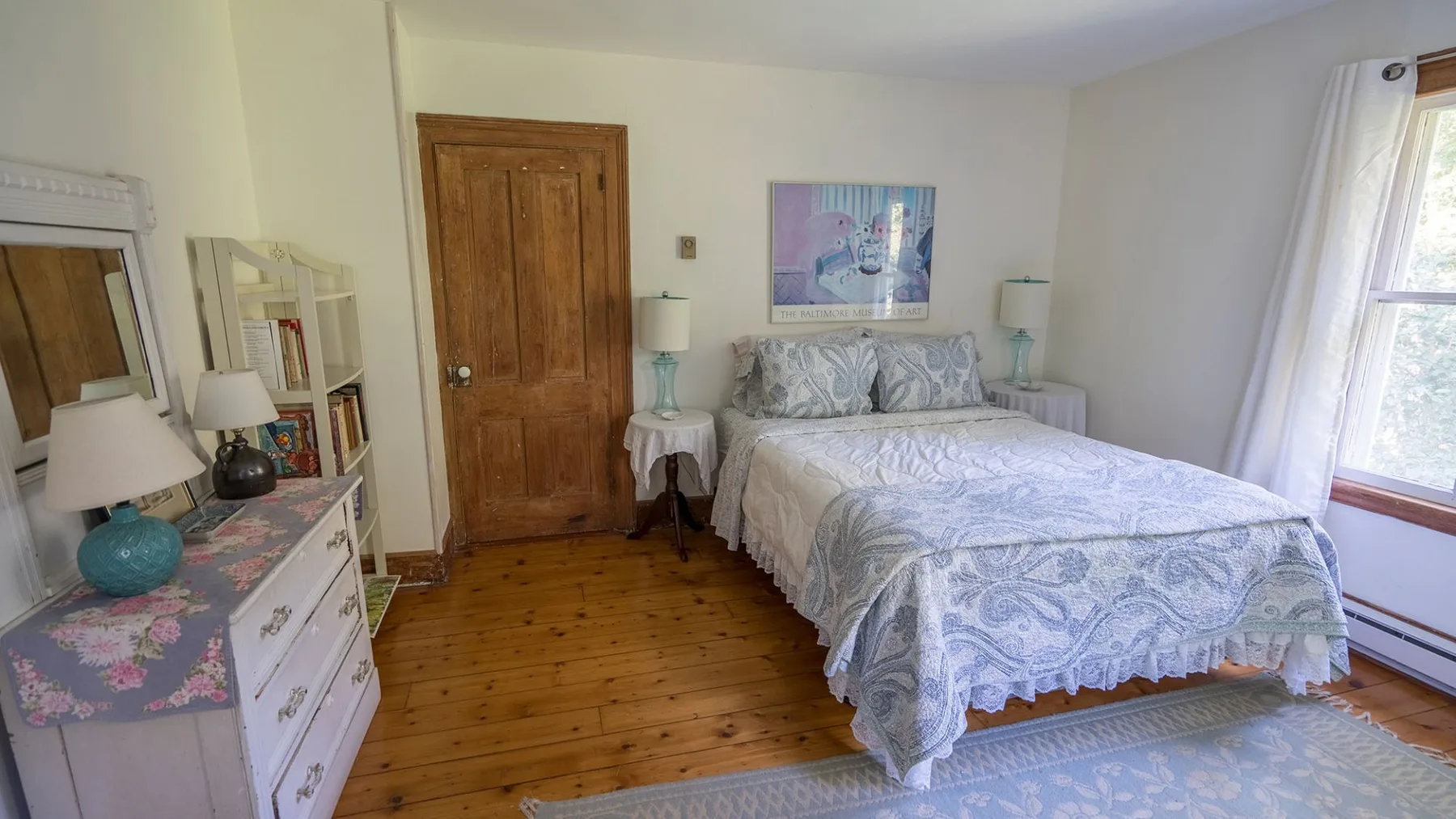 A bedroom with a bed, wooden dresser, and a window with curtains.