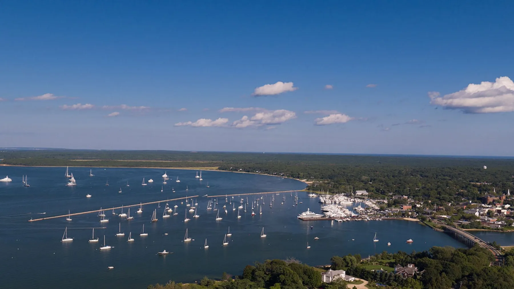 An aerial view of a coastal bay with sailboats anchored near shore.